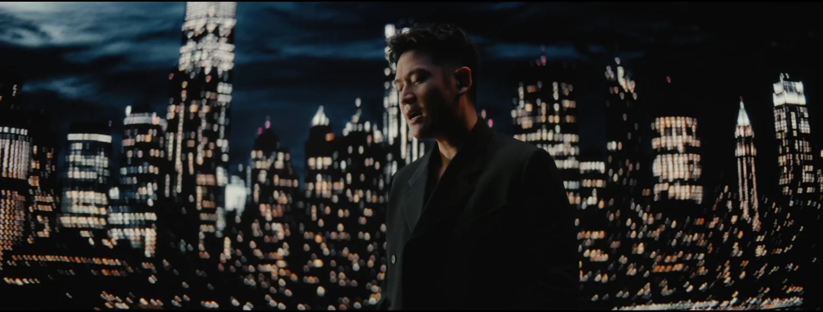 Eric Chou performs against a curved field of illuminated city windows.