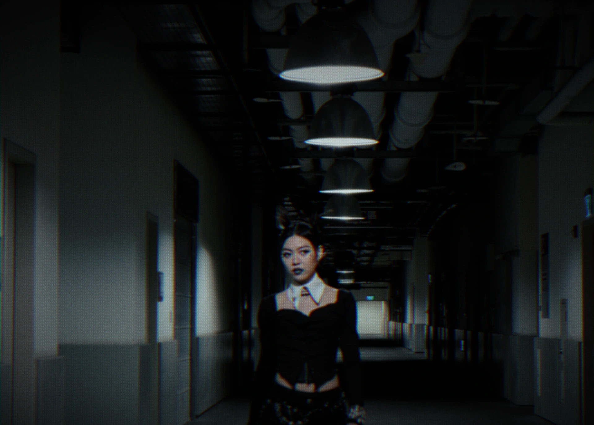 Jasmine Sokko in black beneath the repeating overhead lights of a corridor.