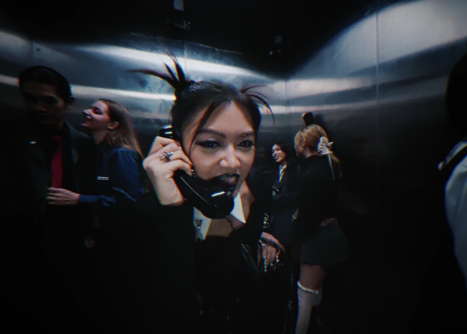 Jasmine Sokko holds a telephone receiver among a crowd inside a metallic elevator.