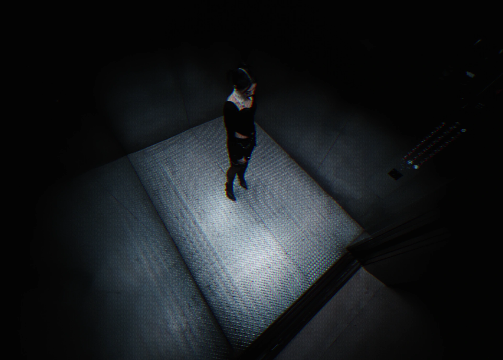A high-angle view of Jasmine Sokko standing on the elevator’s metal floor.