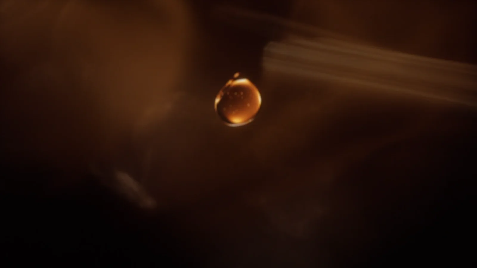 A single amber whisky drop suspended in light