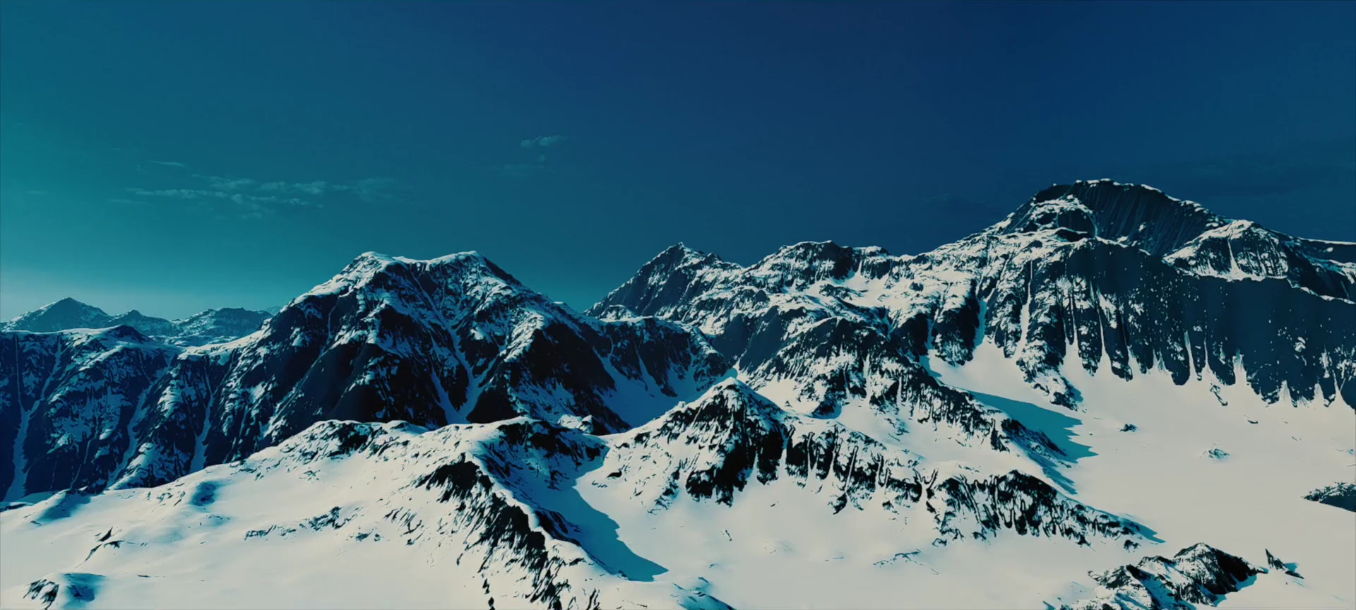 A wide snow-covered mountain range beneath a cyan sky.