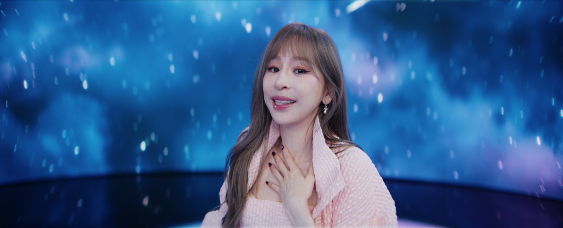 Cyndi Wang in a soft pink jacket against a luminous blue star field.