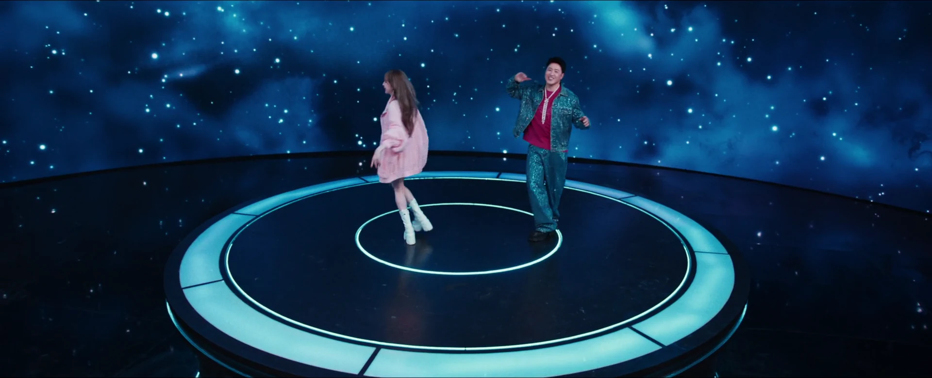 Will Pan and Cyndi Wang sing and dance on a luminous circular stage surrounded by a blue galaxy.