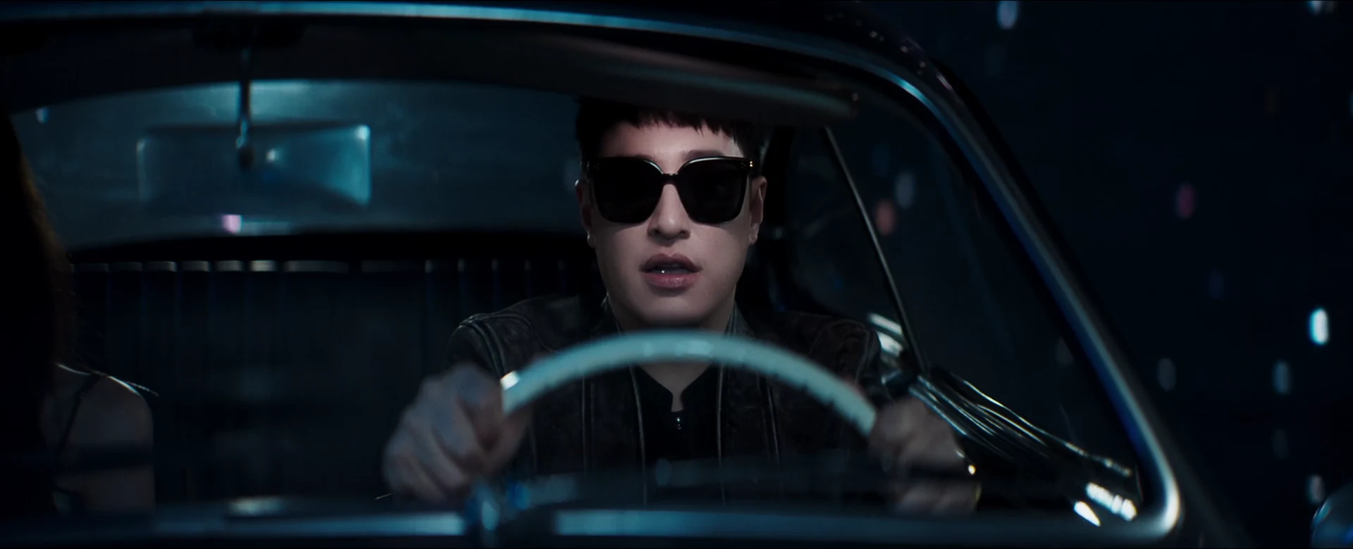 Will Pan wears sunglasses behind the wheel of a vintage car, lit by cyan light.