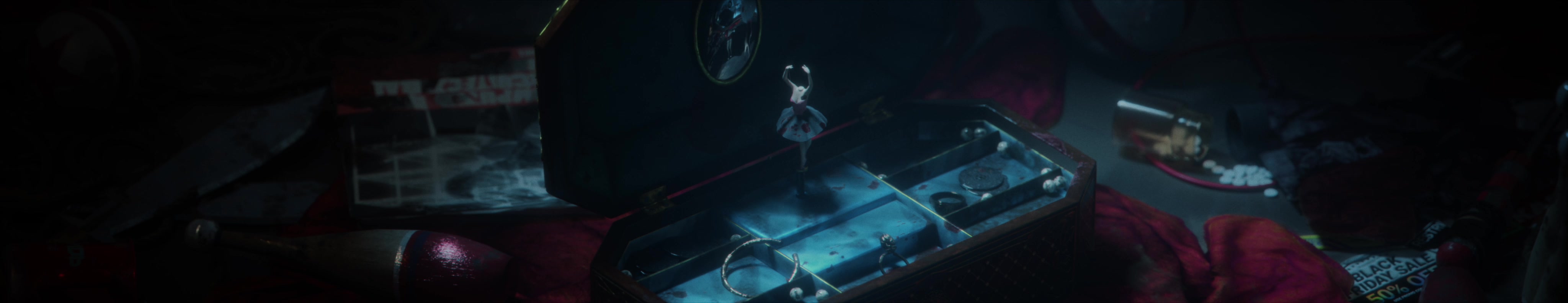 A miniature ballerina stands inside an open music box on red fabric.