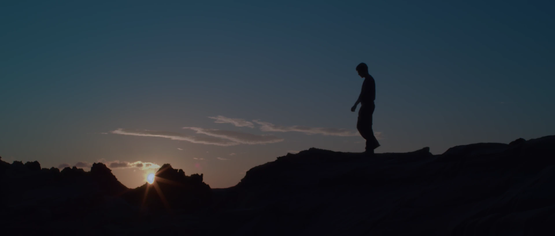 George Hu stands in silhouette on the rocky coast at sunrise.