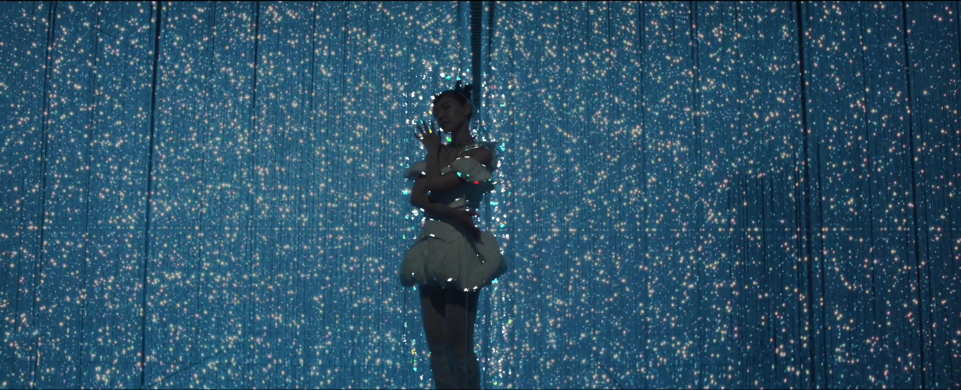 Jasmine Sokko standing amid a blue curtain of lights